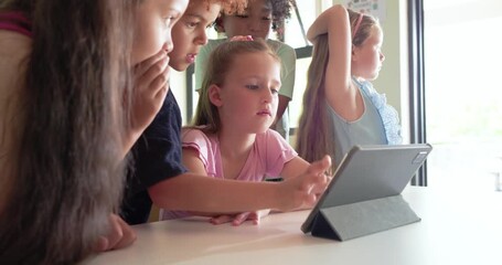 Diverse children clustering at classroom table while girl in pink tapping tablet to share screen - Powered by Adobe