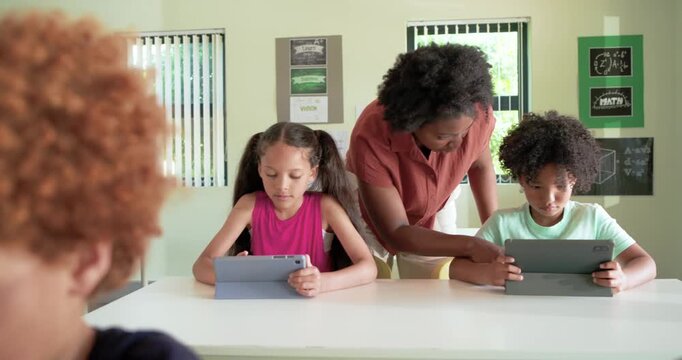 Teacher with students, noticing screens, leaning and adjusting tablet, guiding learning in class