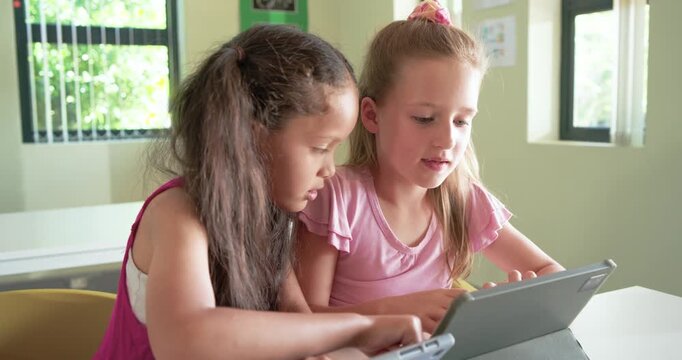 Diverse female pupils leaning in, left child pointing and tapping tablet folio guiding class task