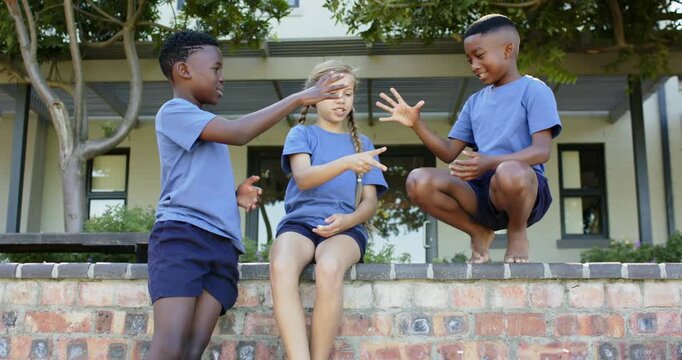 Diverse children starting hand game on brick wall by porch, wearing blue T-shirts and navy shorts