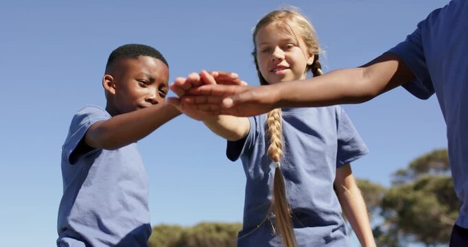 Diverse children in blue tees after girl's braid cue, stacking hands, lifting arms cheering at park