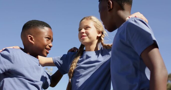 Three preteen teammates huddling, center girl placing arms, giving pep talk on field in blue shirts