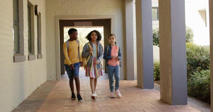 Three preteen students walking down school corridor with backpacks, chatting while heading to class