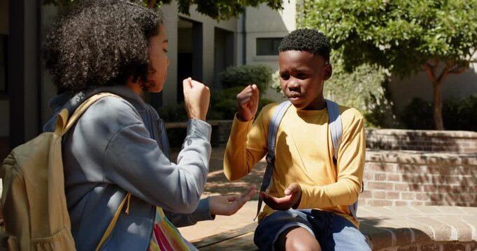 African American teens in courtyard with backpacks, girl initiating hand game, boy replying for fun