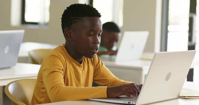 African American child boys reading screen then typing on white laptop in classroom, doing task