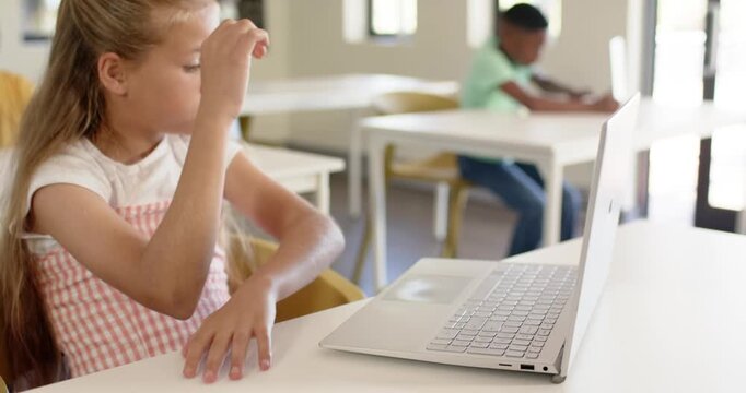 Youth female student reaching, hesitating, typing on laptop in classroom to finish classwork