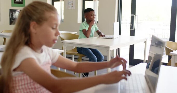 Diverse classmates, female teen typing on laptop in class after glancing at screen to finish work