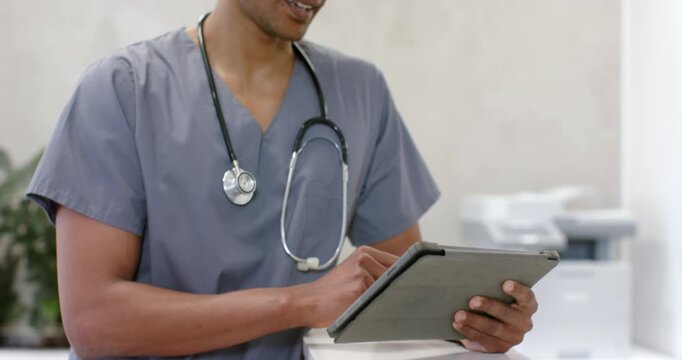 African-American man in grey scrubs stethoscope tapping tablet propped checking chart at reception
