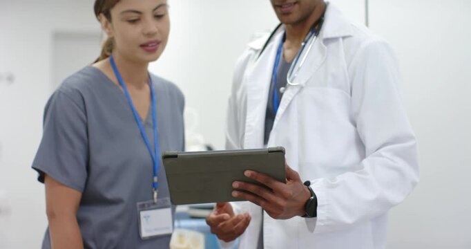 African American doctor and nurse consulting tablet in corridor, doctor gesturing reviewing chart