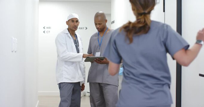 African American medical team reviewing tablet in imaging corridor as nurse rushing about transfer