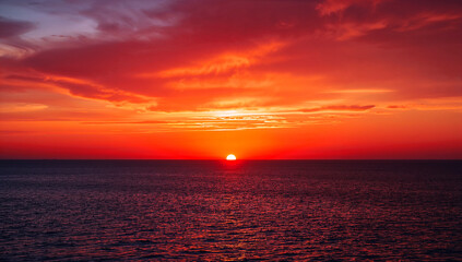 Obraz premium Vibrant sunset over calm sea reflecting fiery sky