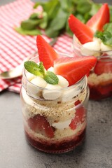 Tasty trifle dessert with whipped cream, strawberries and mint in glass jars on gray textured...