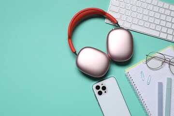 Headphones, computer keyboard, smartphone and stationery on turquoise background, flat lay. Space...