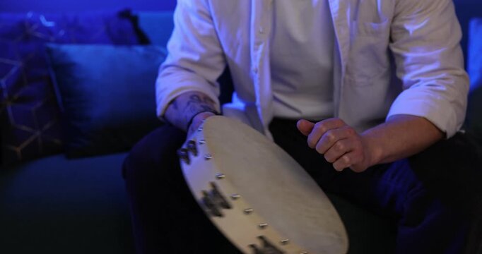 Man playing tambourine in blue light at home, closeup