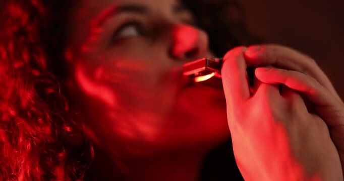 Woman playing harmonica in color lights indoors