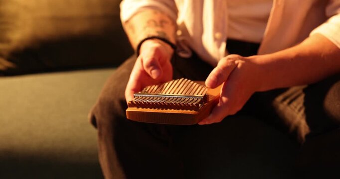 Man playing kalimba on sofa at home, closeup. Camera moving right