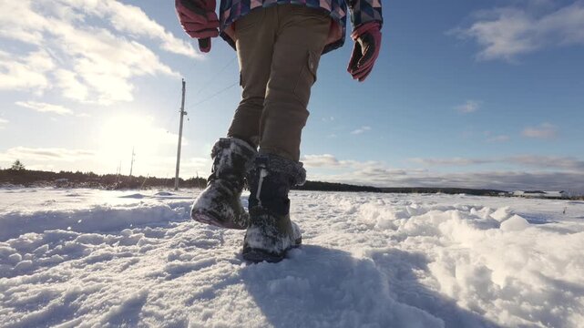 Rear view of teenage girl legs wearing winter boots walking on fresh snow. Winter scene in Nova Scotia, Canada, cold season atmosphere, outdoor lifestyle and calm snowy landscape.