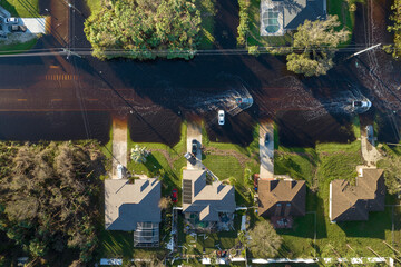 Flooded Florida road with evacuating cars and surrounded with water houses in suburban residential area. Consequences of hurricane natural disaster