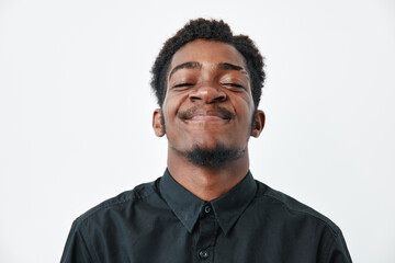 Fototapeta premium Young African American man with dark skin and short hair smiling with closed eyes wearing black shirt on white background. Portrait, happiness and confidence concept.
