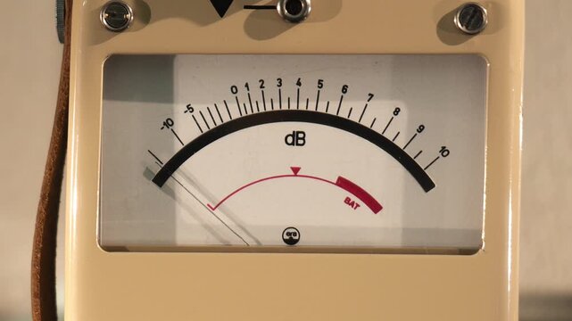 Analog decibel meter gauge on a vintage sound level measuring device, closeup detail of dB scale and indicator needle for audio loudness and noise monitoring equipment