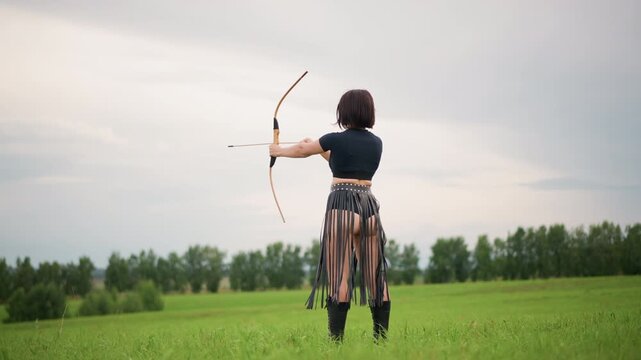 Lone archer stands on grassy field, leather skirt and bow raised against cloudy horizon, nocking and releasing arrow across wind, cinematic solitude, focused stance and quiet strength.