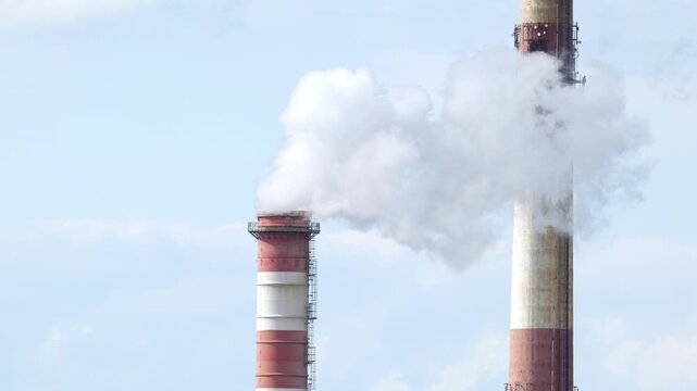 Steam plume rising from red and white striped industrial chimney against clear blue sky, closeup side view of factory smokestack emissions, air pollution and energy production concept, no people