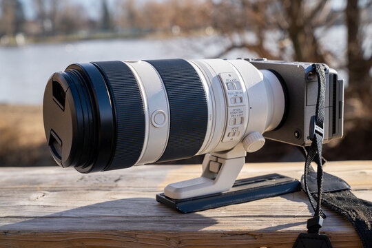 Close-up view of a professional mirrorless camera paired with a large telephoto zoom lens resting on a wooden surface outdoors.