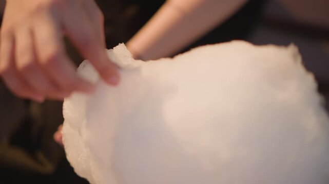 evening street hands pulling cotton candy, closeup on fingers shaping fluffy sugar cloud with warm bokeh lights, vendor apprentice crafting delicate strands, soft tactile motion, moody market