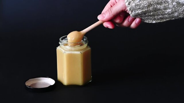 Person using a Honey Dipper to Scoop Creamed Honey, black background