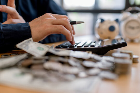 Man calculating personal budget with calculator, coins and dollar banknotes on table. Financial planning, saving money, expense control, household finance management and economic responsibility concep