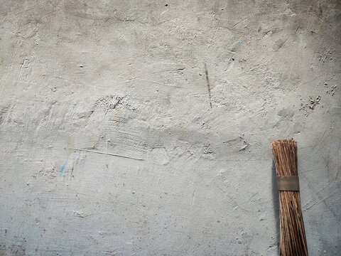 traditional wooden broom leaning against a rough weathered gray concrete wall