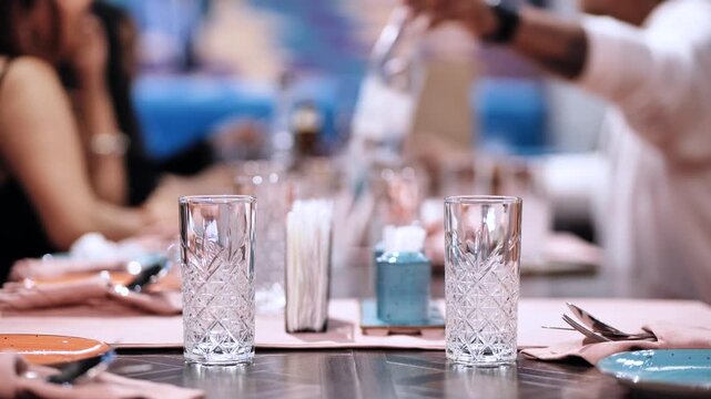 Dinner table setting with empty glasses, people enjoying a social gathering at a restaurant