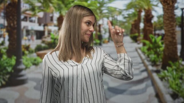 Woman pointing finger under vibrant green palm trees on a sunny busy pedestrian street; direction confidence.
