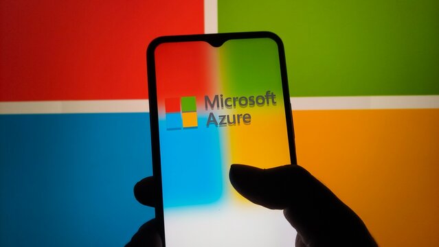 A hand holding a smartphone with the Microsoft Azure logo on the screen in front of a colorful background