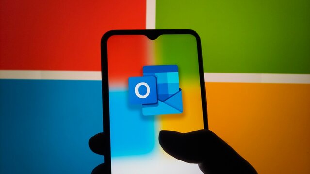 A hand holding a smartphone with the Outlook app on the screen in front of a colorful background