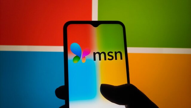 A hand holding a smartphone with the MSN logo on the screen in front of a colorful background