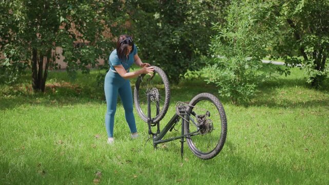 woman adjusting bicycle wheel on lawn with upright bike and open spokes, bright daylight and lush green grass, practical toolkit at feet, commuter vibe turning into quick success, visible chain