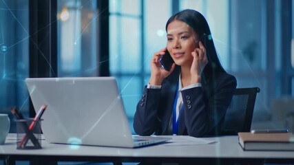 A professional woman in a dark blazer, using a cell phone, while sitting at a desk with a laptop - Powered by Adobe