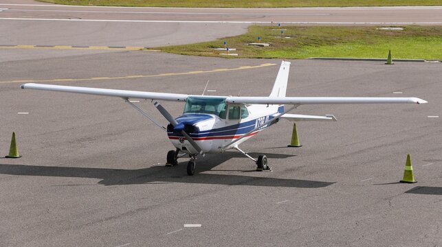 St Petersburg, Florida, U.S - Jan 2, 2026 - A white Cessna 172 with blue and red stripes parked near yellow taxiway cones at Albert Whitted Airport