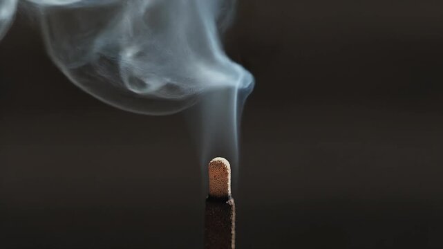 A slender incense stick steadily burns, releasing a graceful column of white smoke against a dark background.