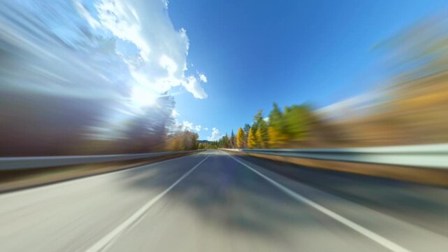 The Car Rushes Along a Forest Road Under a Bright Blue Sky With Fluffy Clouds. Sunny Day. Sort of Dashcam POV. Road Trip Travel Concept. Trees Turning Into Abstract Blur. Hyperlapse