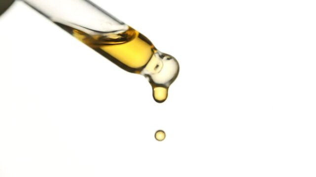 Yellow liquid dripping from a glass dropper onto a white background