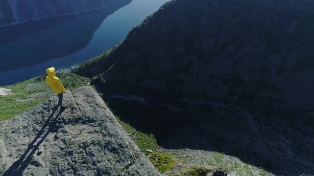 Cinematic view of woman on rocky edge overlooking fjord in Norway
