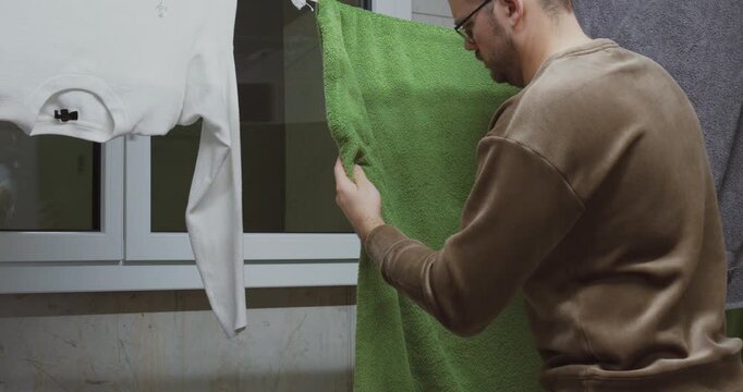 A man smells freshly washed laundry indoors and reacts with frustration as it still smells unpleasant. Concept of household problems, odor issues, ineffective washing, and everyday domestic challenges
