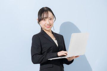 水色背景でパソコンを持つスーツの若い女性　新卒や就職のビジネスイメージ　就活の採用イメージカメラ目線