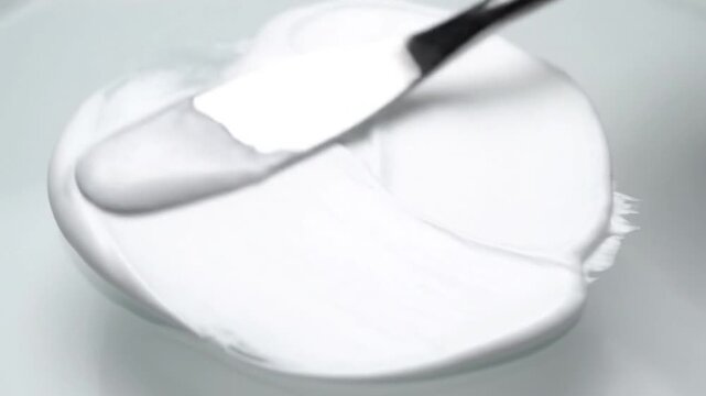 A palette knife swirls thick white paint, creating smooth textures and curves