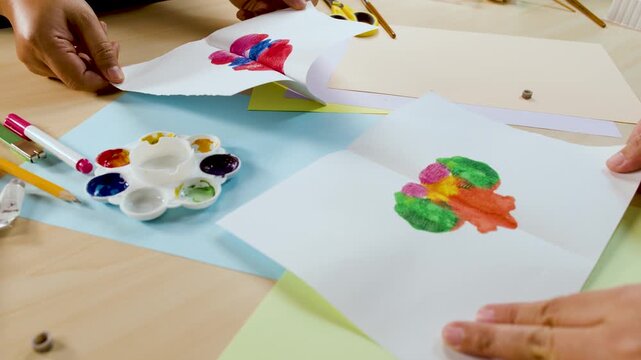 Hands Creating Symmetrical Abstract Art with Colorful Paint on White Paper