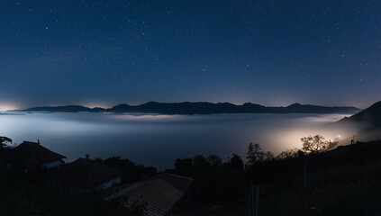 Naklejka premium 星が薄れゆく未明、月光の銀に染まる雲海と黒い屋根が連なる静寂の谷、人物なし
