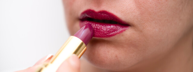 Naklejka premium Girl paints her lips with bright lipstick on a light background