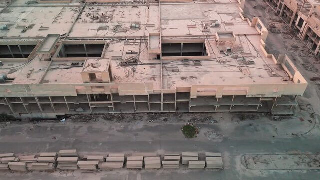 Drone aerial of an unfinished concrete complex with rooftop wiring, open shafts, empty street corridor and scattered rubble&mdash;stalled construction site ideal for industrial, safety, and real estate them